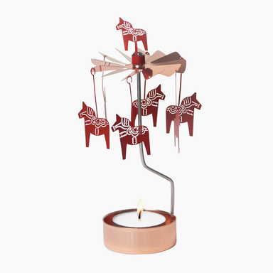 A copper-colored metal wind spinner ornament featuring five hanging Swedish Dala horse cutouts and a lit tea light candle in a matching round holder, set against a plain white background.