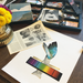 Collection of vintage items including a color chart, feathers, and a box of postcards on a wooden surface.