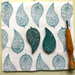 Two carved leaf-shaped carved blocks with teal printed patterns displayed on a white fabric with a wooden carving tool.