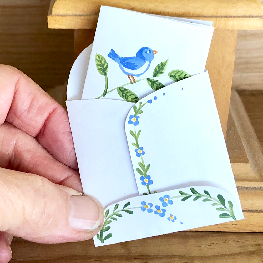 Hand holding a small folded card with a blue bird illustration on a wooden surface