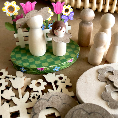 Wooden figurines unpainted and decorative elements on a checkered base with flowers and a fence.