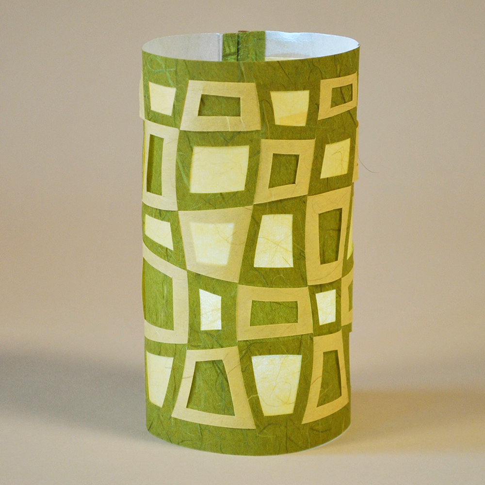 Green and white geometric patterned cylindrical paper lamp on a beige background