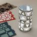Cylindrical paper lantern with geometric cutouts on a light gray background with three additional lamp samples shown flat