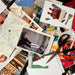 Collage materials of vintage paper cutouts, printed cards, a black-and-white photo print, a map, scissors, and craft supplies arranged on a dark surface.