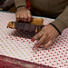 Block printing in studio- pink background with hand holding block priting flowers