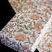 Block printed foral flowers with green leaves on white background used to wrap a gift and shown with flat sheet