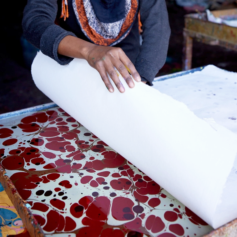 Artist placing blank sheet of paper on marbled pattern floating on water.