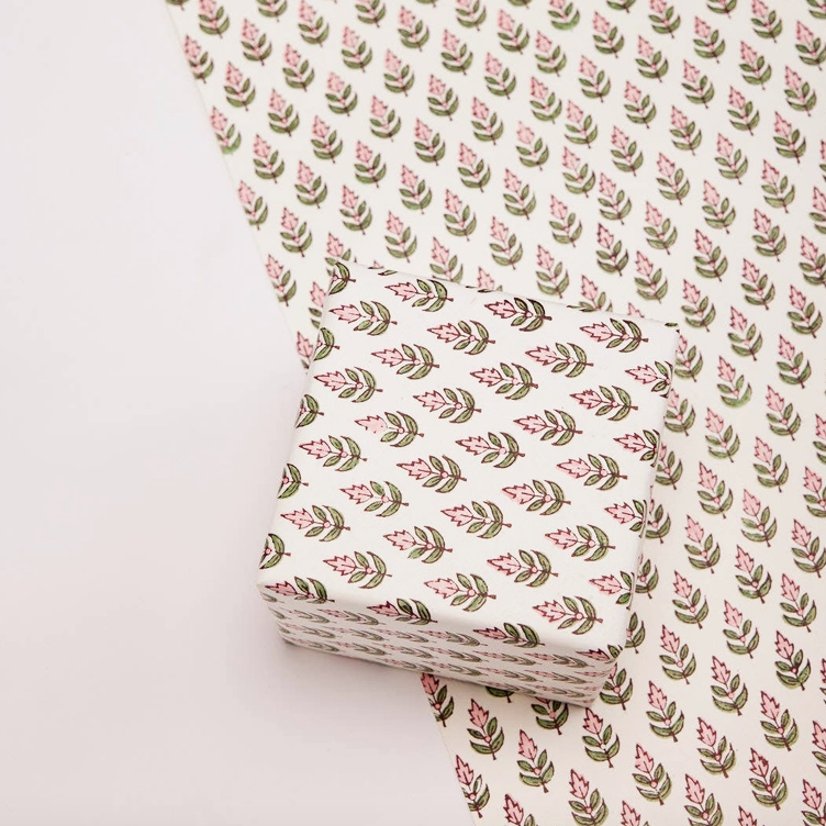 paper with repeating pink and green floral pattern on a white background with one flat sheet and a box wrapped with the same paper