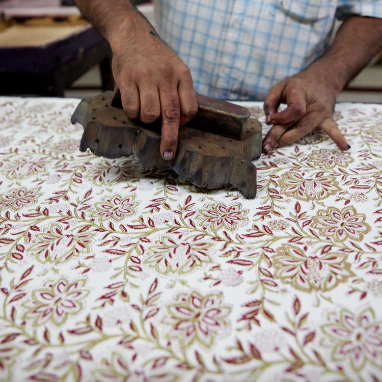 Person using a wooden block to print floral patterns on paper.
