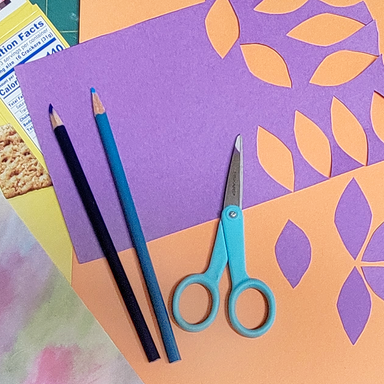Purple paper with orange leaf patterns, blue scissors, black and blue pencils on a colorful background