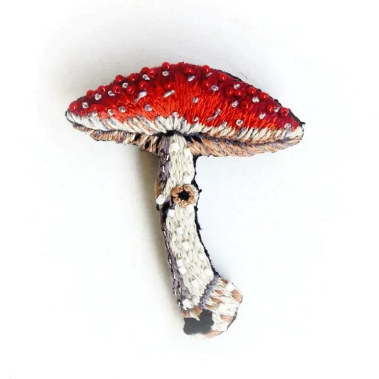 Mushroom-shaped brooch with red cap and white stem on a white background