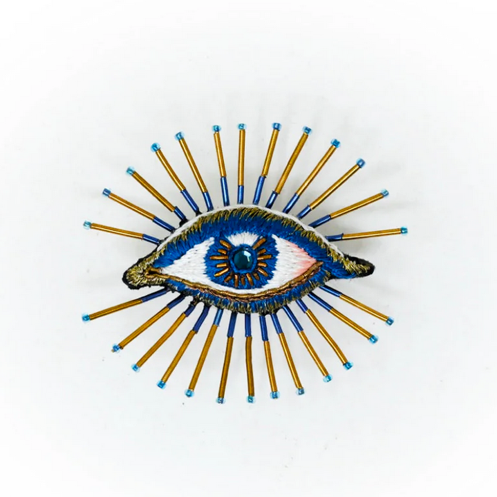 Decorative beaded brooch with an eye design on a white background