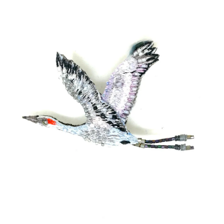Sanhill Crane in flight beaded brooch with metallic sheen on a white background