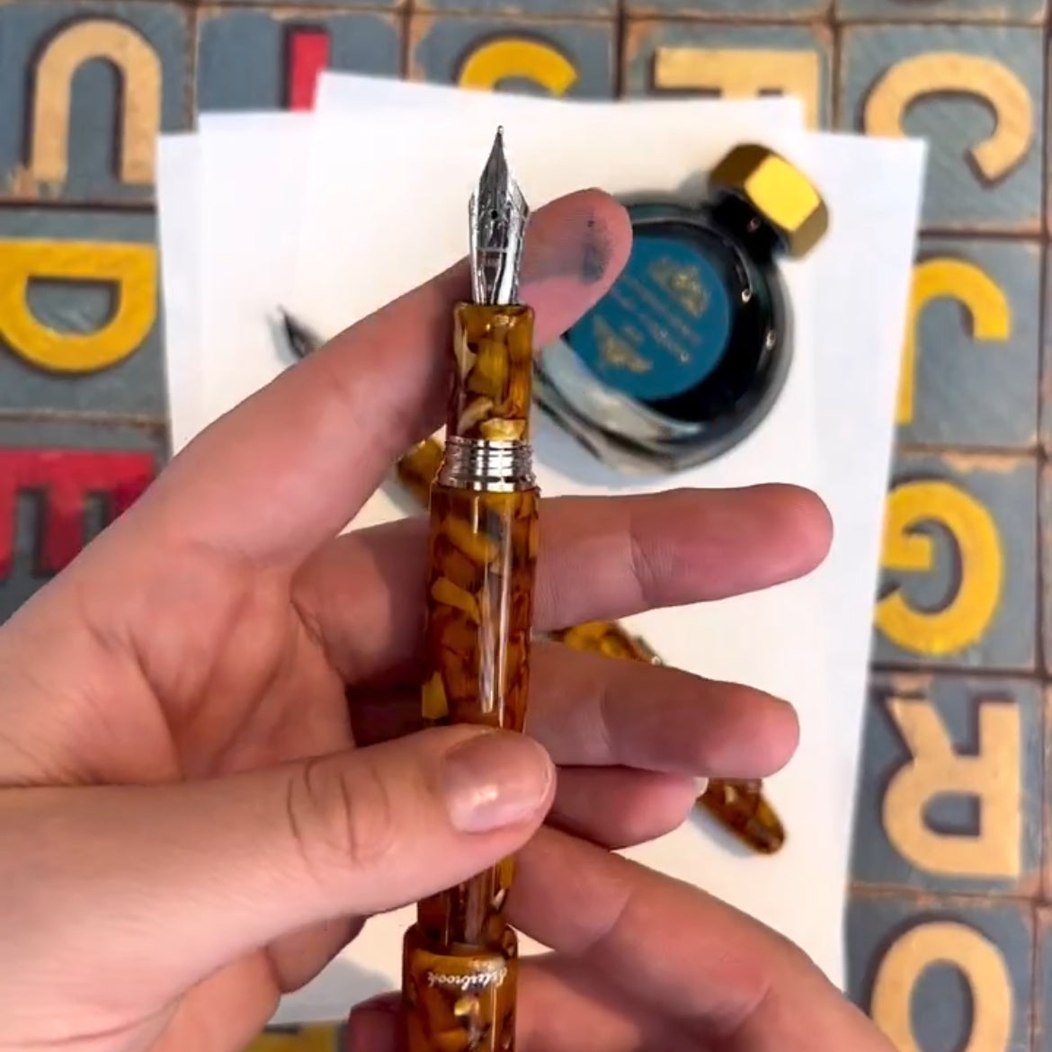 Hand holding a tortoiseshell fountain pen with ink bottle in the background