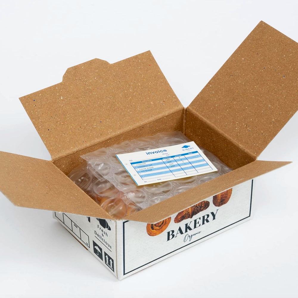 Open cardboard box with a bakery design, containing packaging and an invoice on a white background.