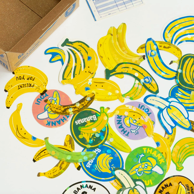 Collection of banana-themed stickers on a white surface with a cardboard box in the background.