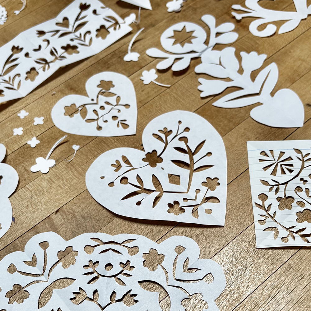 White paper cut decorations with floral and heart patterns scattered on a light brown wooden floor.
