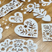 White paper cut decorations with floral and heart patterns scattered on a light brown wooden floor.