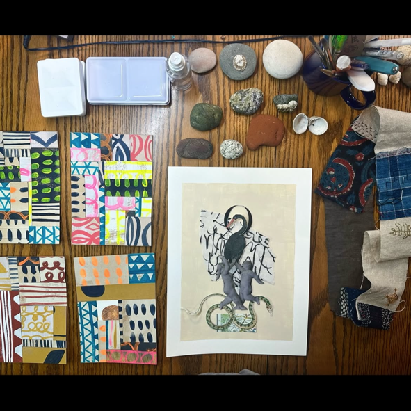 Collage featuring a black and gray bird on a beige background with a white border, displayed on a wooden table surrounded by colorful patterned paper swatches, stones, shells, and art supplies.