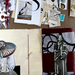 An open mixed-media collage book  layout spread on a brown surface, showing layered papers, photographs, fabric, ink marks, and collage elements including a stork print, a nautilus shell, a black-and-white portrait, and deep red and cream sections.