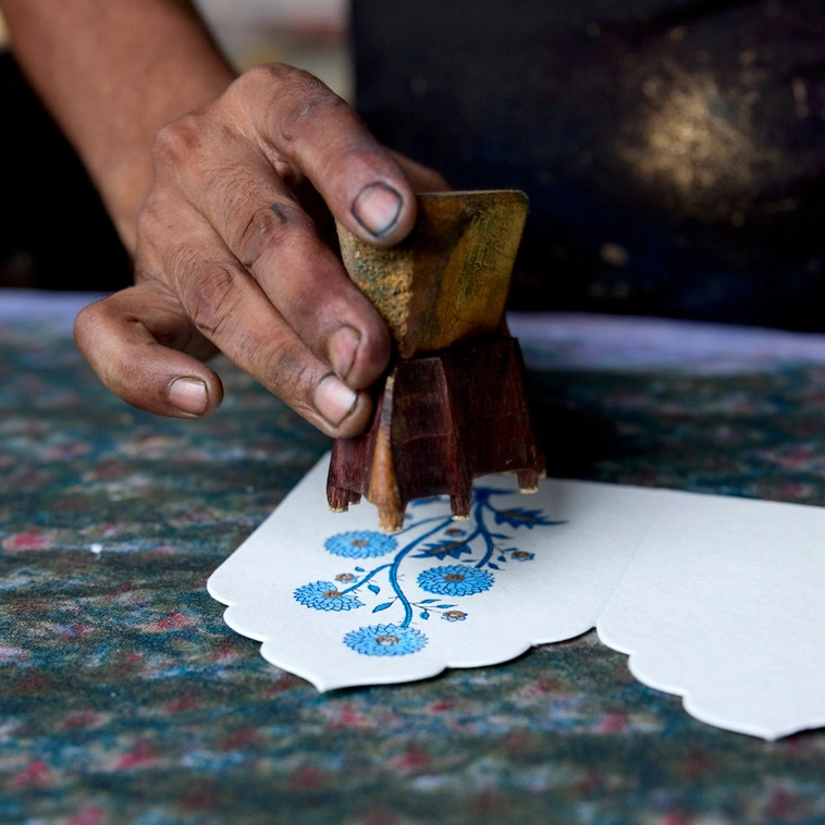 Hand using a wooden printing block with floral design on paper.