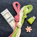 Japanese embroidery thread set with pink, cream, and light green threads, a box of needles, a green thread cap, and a pink flower-shaped stitch holder on a dark denim background.