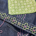 Close-up of a handmade patchwork fabric featuring dark blue denim with pink and lime green embroidery, a light green patch with white star stitching, and a sewing needle resting on the surface.