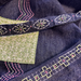 Close-up of a dark indigo denim fabric with colorful hand-stitched patterns, including a green patch with white stitching and a black embroidered trim.