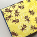 An open book featuring a yellow background with a pattern of brown and black bees and white hexagonal honeycomb cells, finished with a dark blue and white dotted border.