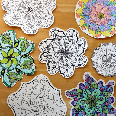 A collection of cut mandala designs displayed on a light wooden background. Some mandalas are black and white line art, while others are colorful and filled with shades of green, blue, purple, pink, and yellow.