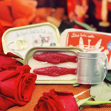 Tinned Fish Candle- Smoked Rose Water 2 red wax fish in tin shown with roses