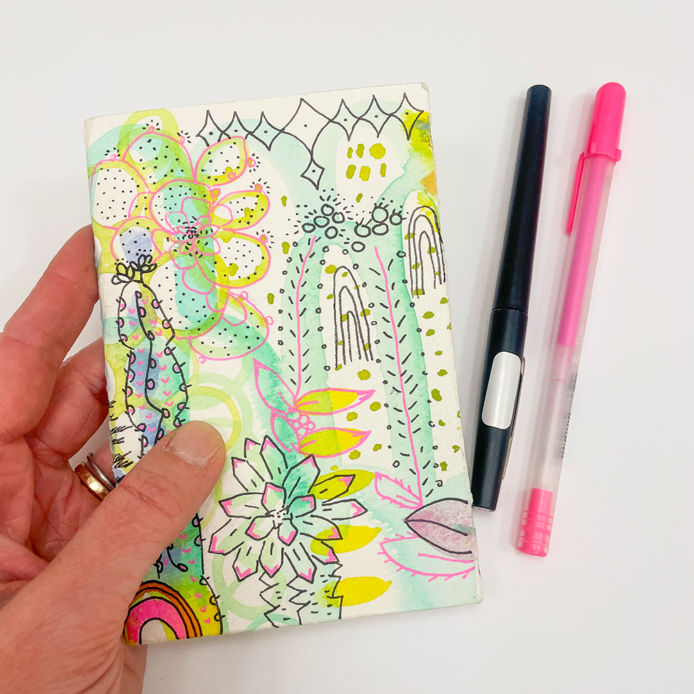 Artzine - Ready, Set, Draw! hand holding page sample with rainbow and geometric drawings and pens