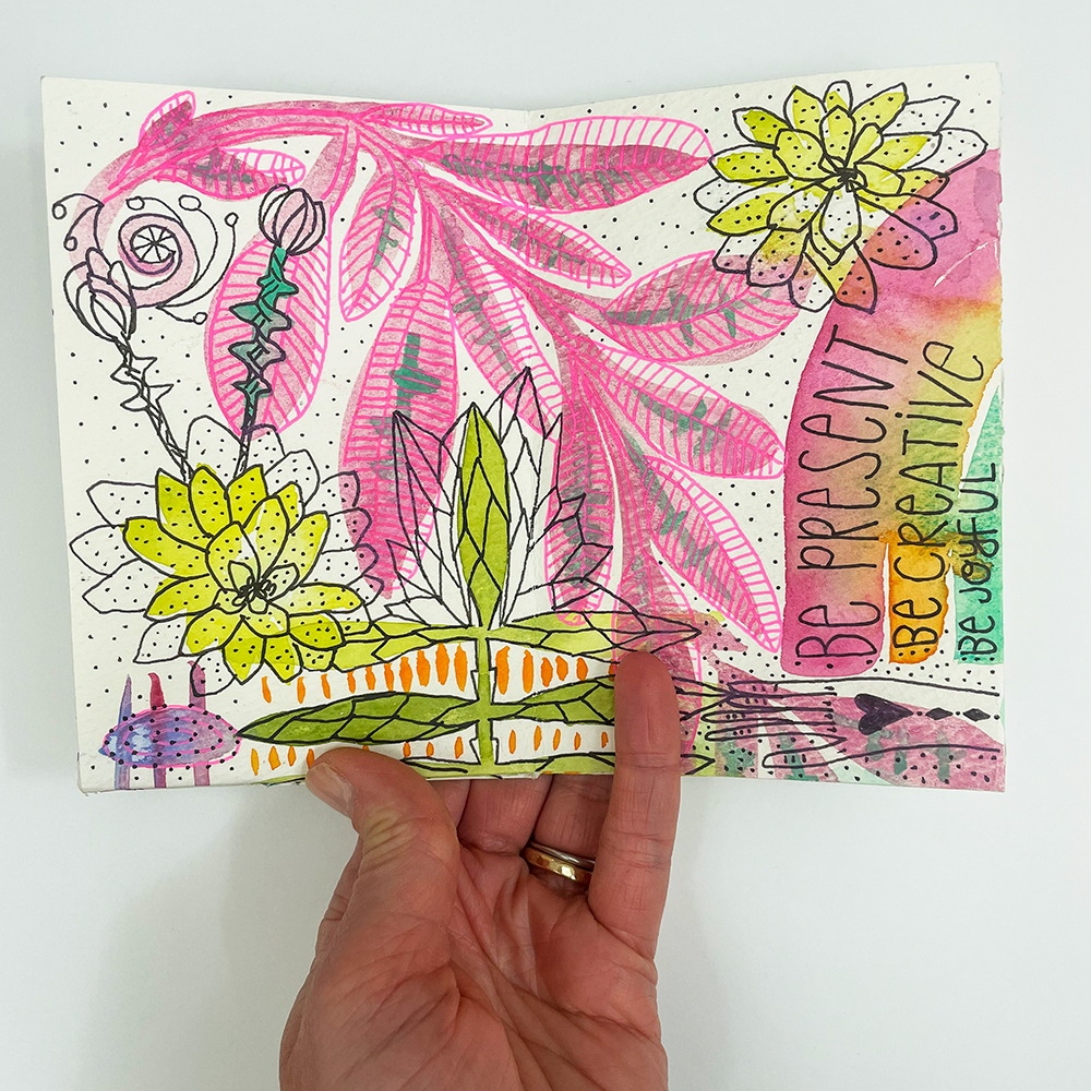 Artzine - Ready, Set, Draw! hand holding page sample with rainbow and pink leaf drawing "Be present, be creative, be joyful"